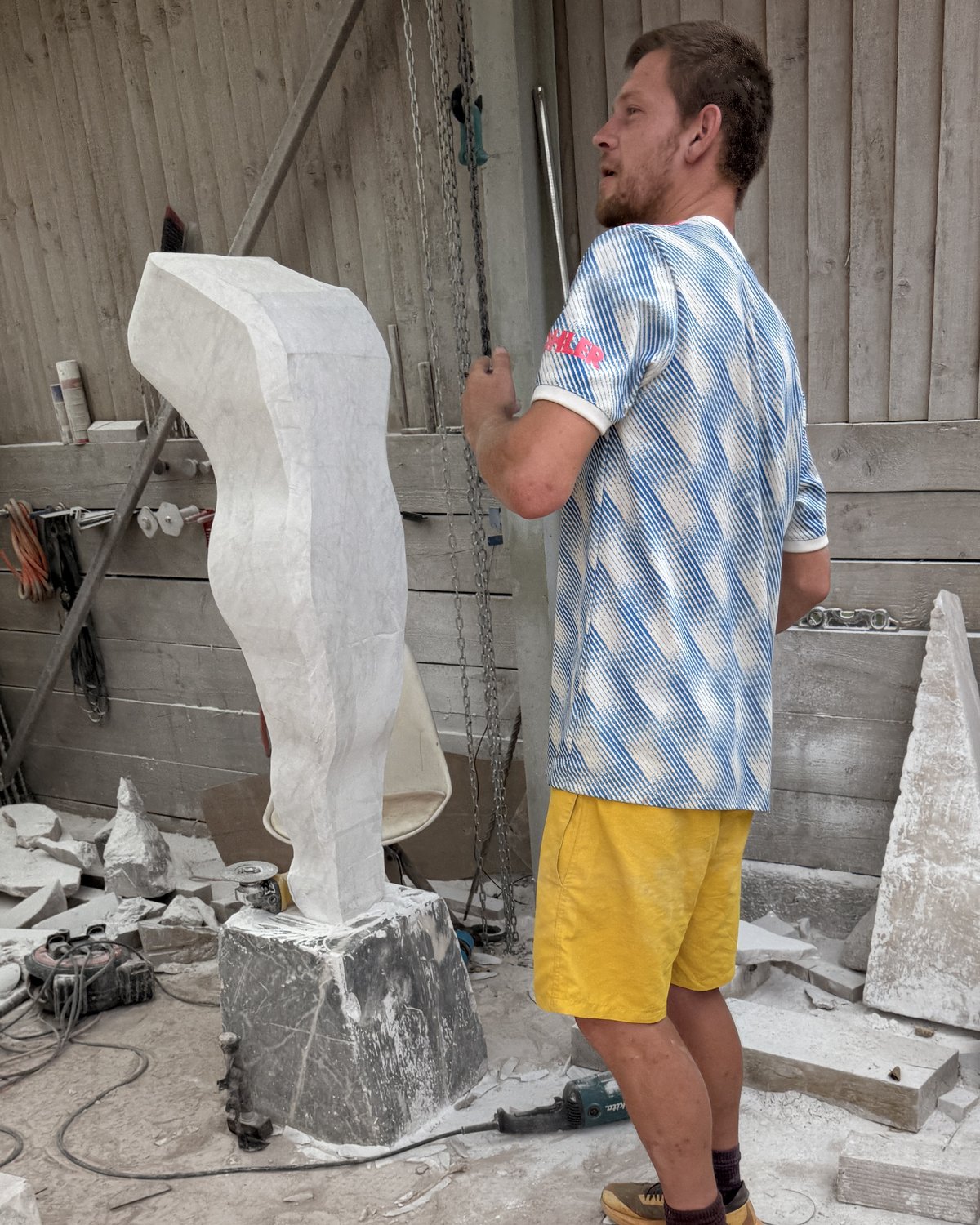 Zak steadying the hoist chain beside the figure, roughed out in white marble and standing on a block in the workshop