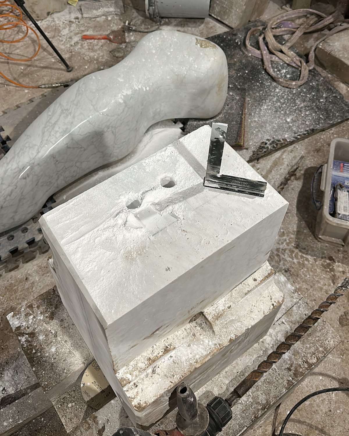 The polished figure lying on mats beside a block of white marble drilled with two holes, a set square resting on top
