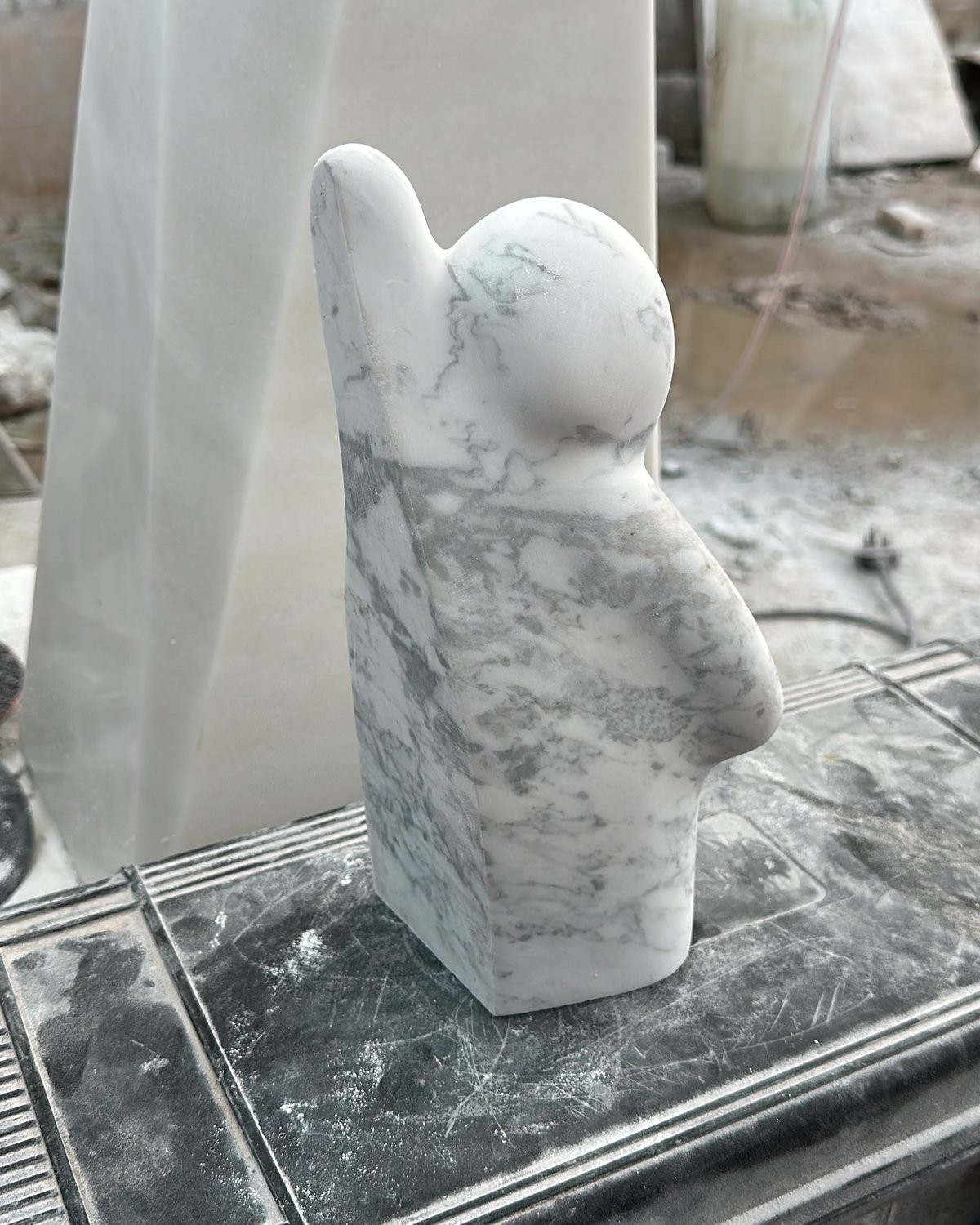 The small companion figure in the workshop, seen from behind: a round head, a raised arm and a flat back