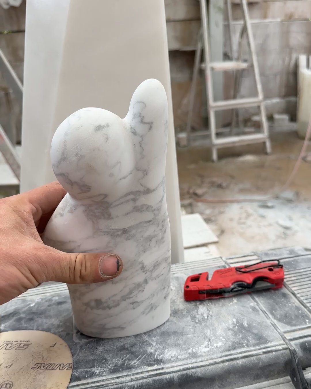 A hand holding the small marble companion figure in the workshop